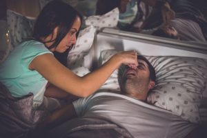 woman holding man's nose in bed 