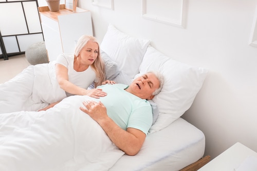 Mature irritated woman in bed with snoring husband