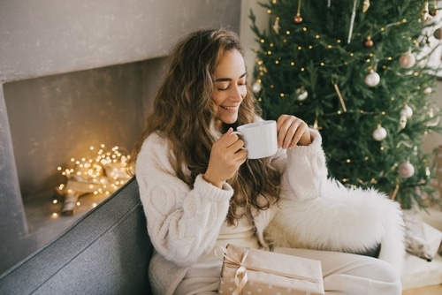woman drinking coffee on couch with Christmas tree.