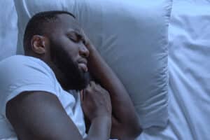 Anxious man suffering from nightmares and sleep apnea, tossing in bed while experiencing bad dreams